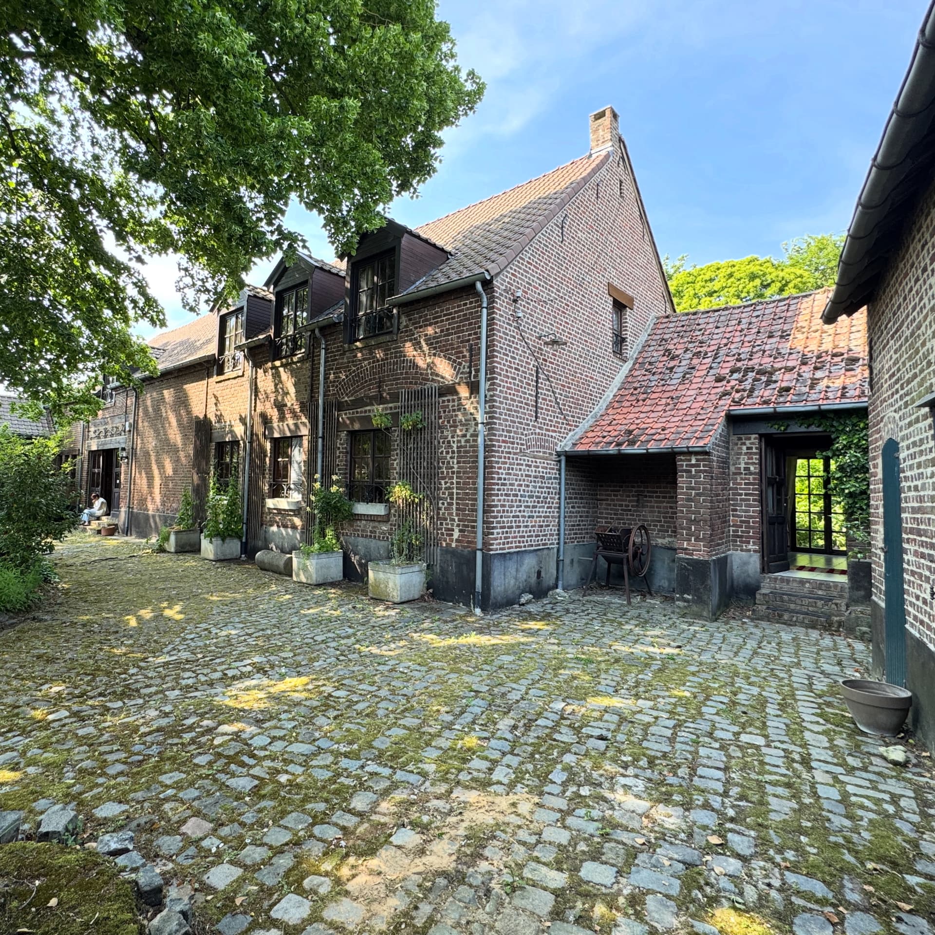 Behind the scenes: bestaande hoevegebouwen van Modern Manoir Chique met kasseikoer en bakstenen gevels voor de renovatie.